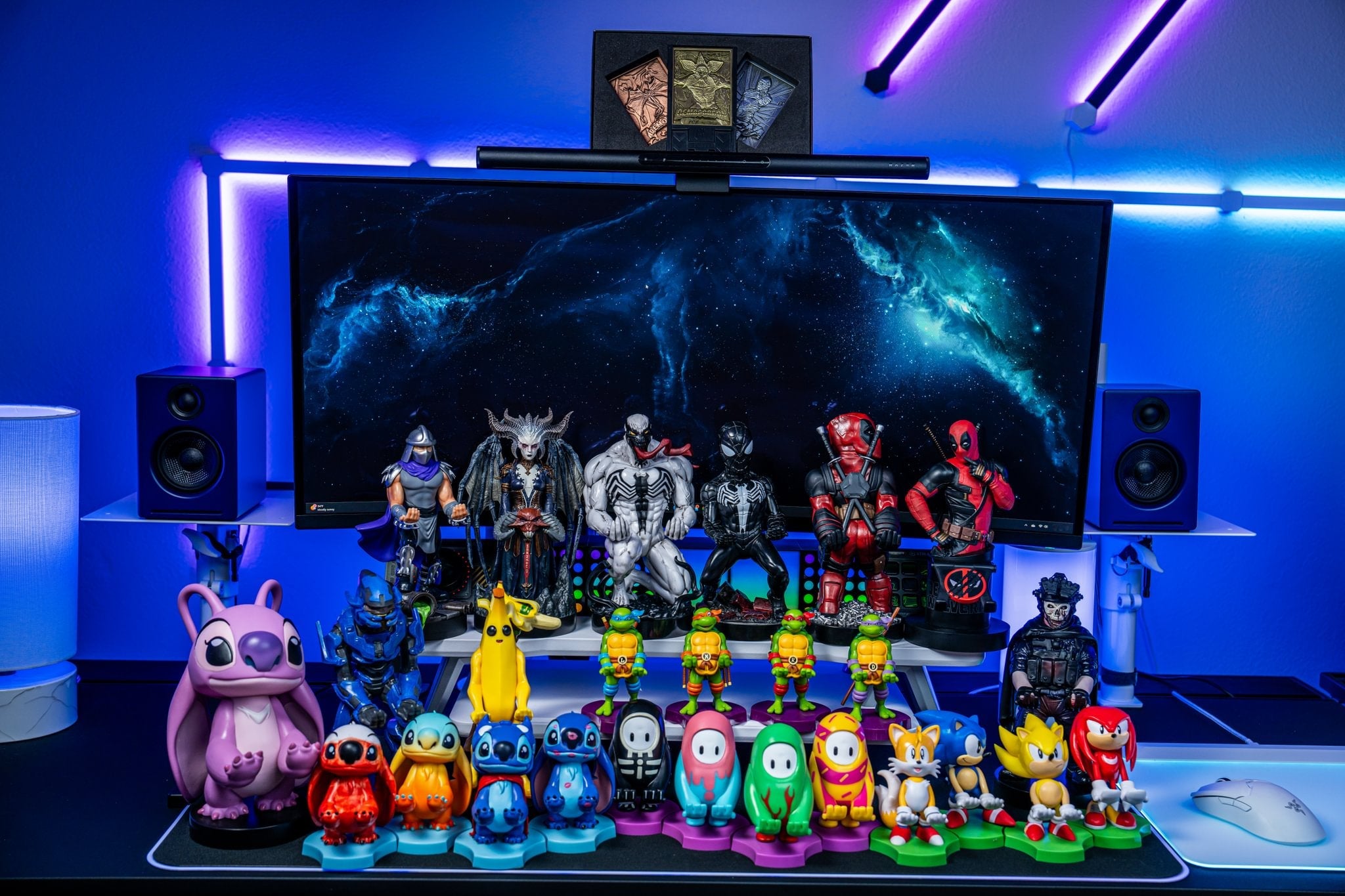 Collection of Cable Guys and Mini Cable Guys featuring characters from Marvel, Halo, Pokémon, Sonic, Fall Guys, Teenage Mutant Ninja Turtles, and Stitch displayed on a gaming desk with RGB lighting.