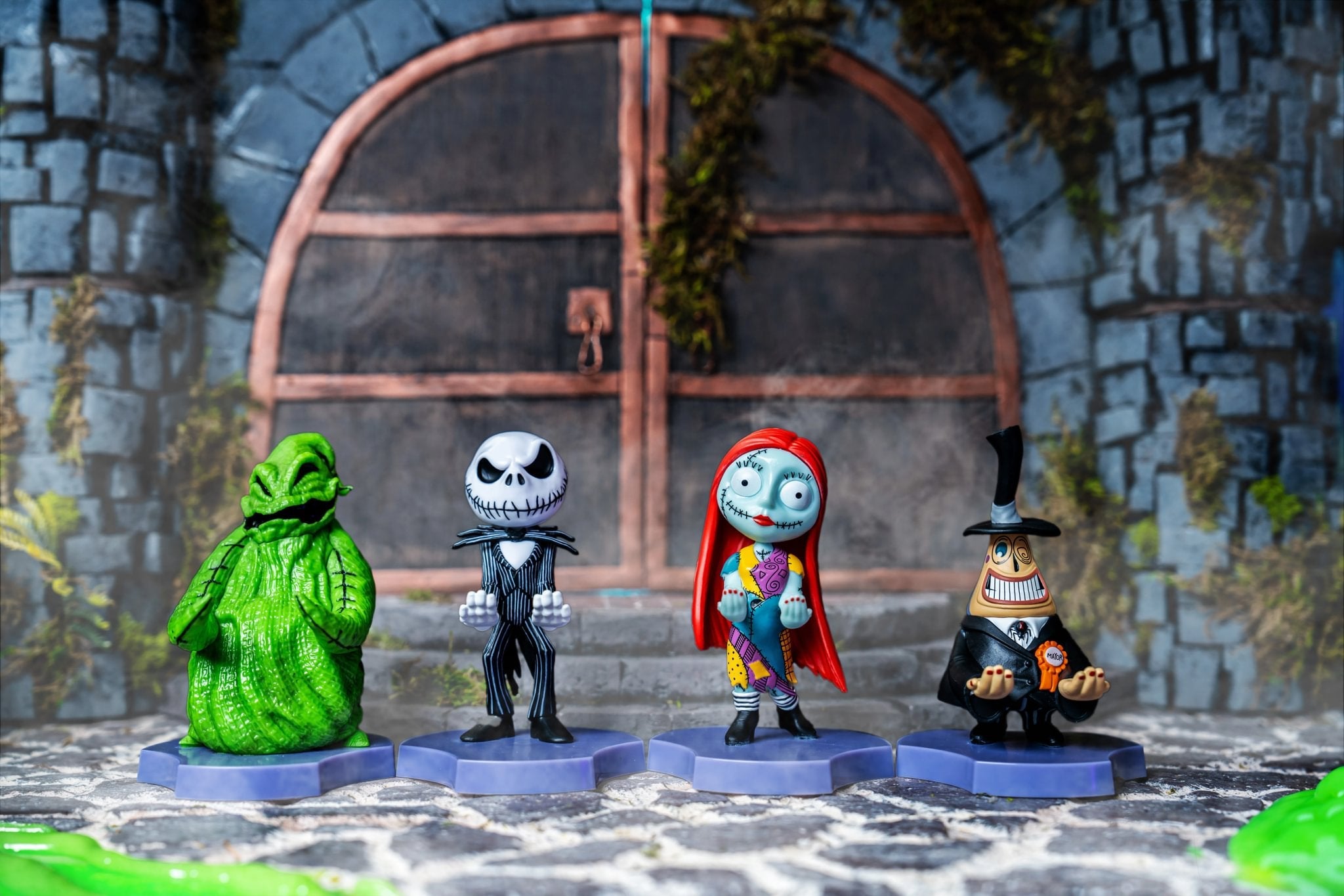 The Nightmare Before Christmas Cable Guys collection featuring Oogie Boogie, Jack Skellington, Sally, and the Mayor figures displayed in a spooky courtyard setting.
