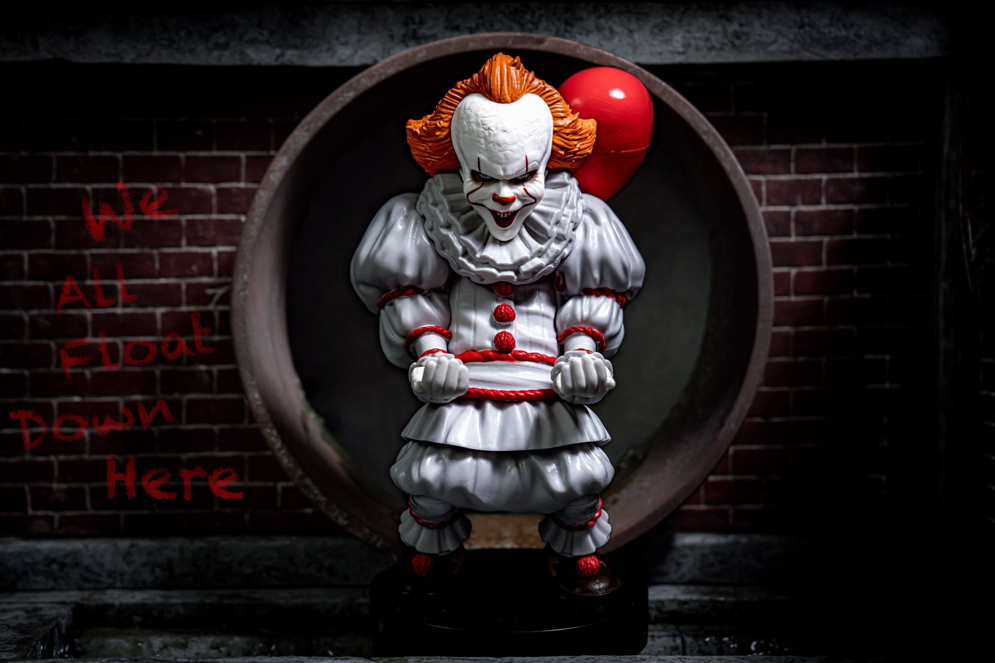 Pennywise Cable Guy figure displayed in a dark sewer-themed setup with the phrase “We All Float Down Here” written on the brick wall in the background.