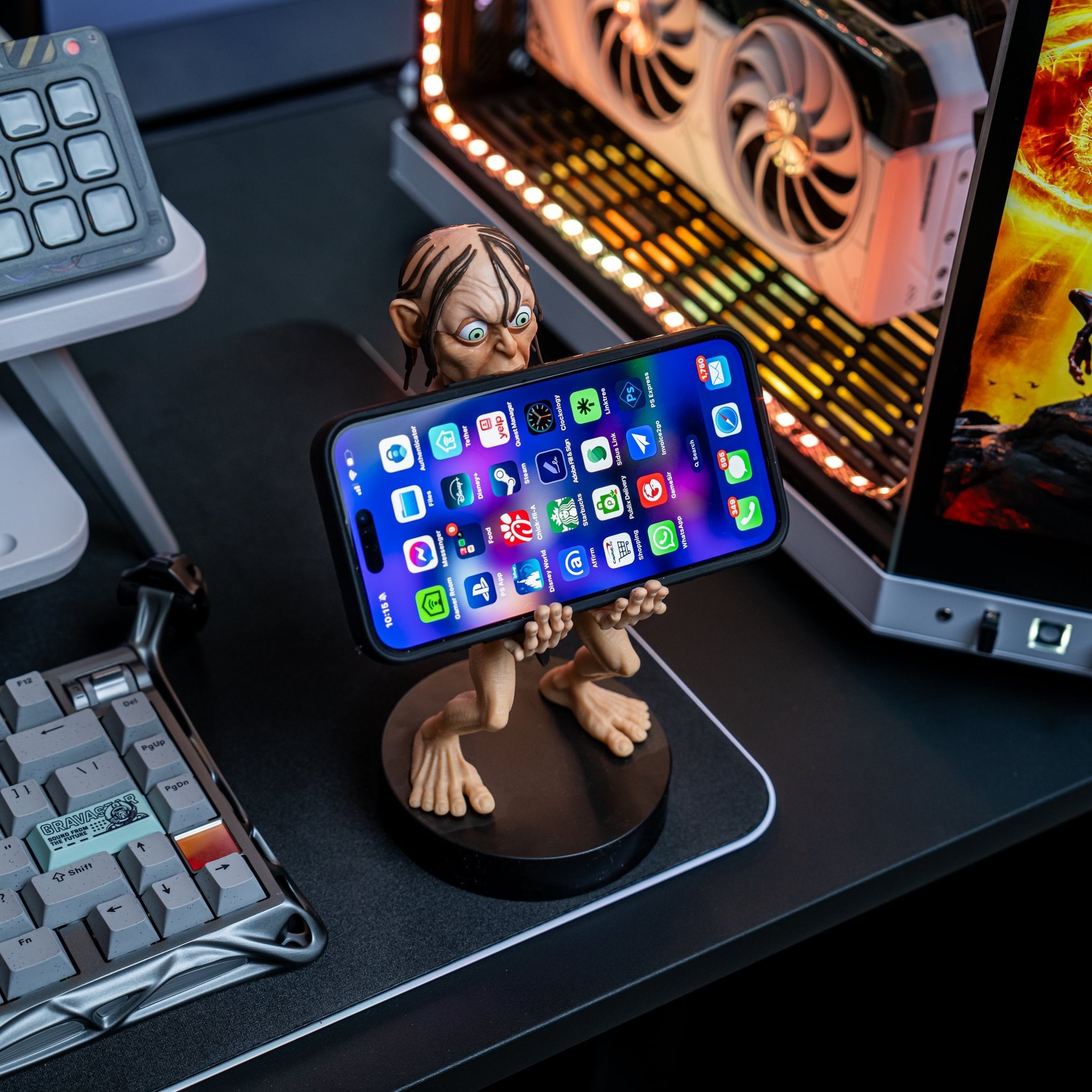 Gollum Cable Guy holding a smartphone on a gaming desk setup with a mechanical keyboard, RGB lighting, and a computer in the background.