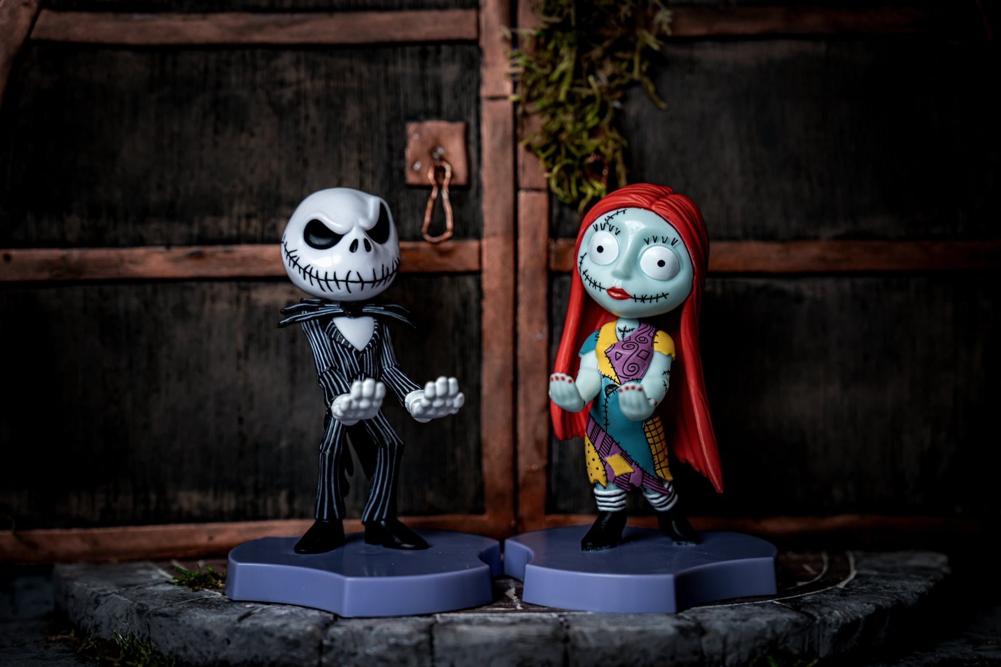 Jack Skellington and Sally Mini Cable Guy holders from The Nightmare Before Christmas, displayed together on matching purple bases in front of a dark, wooden door background.