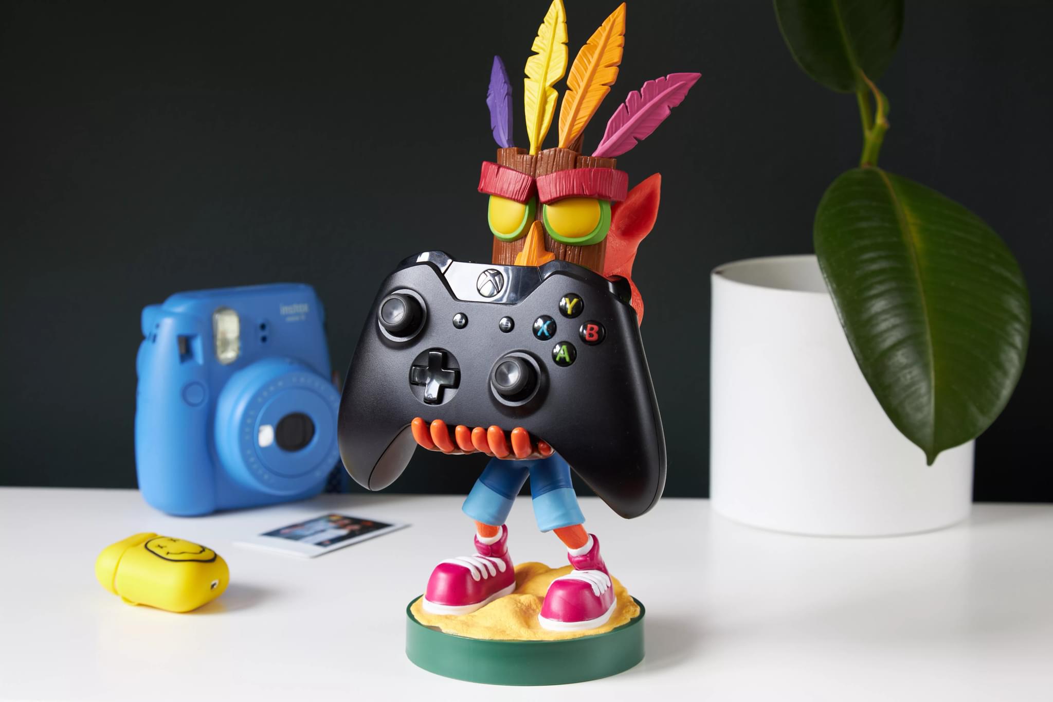 Aku Aku Cable Guy from Crash Bandicoot holding an Xbox controller on a white desk with a retro-themed setup.
