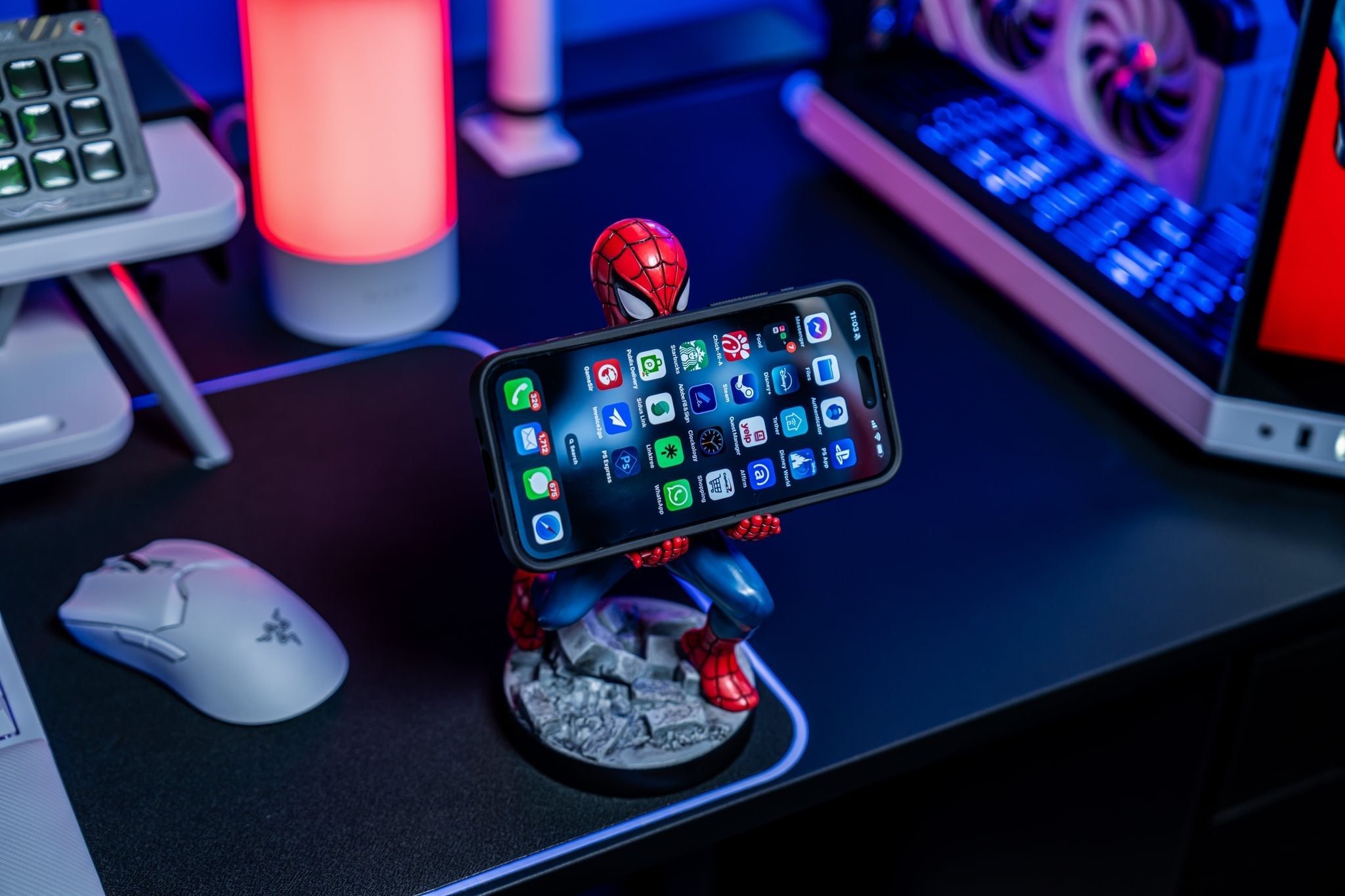 Spider-Man Cable Guy holding a smartphone on a gaming desk setup with RGB lighting and computer accessories.