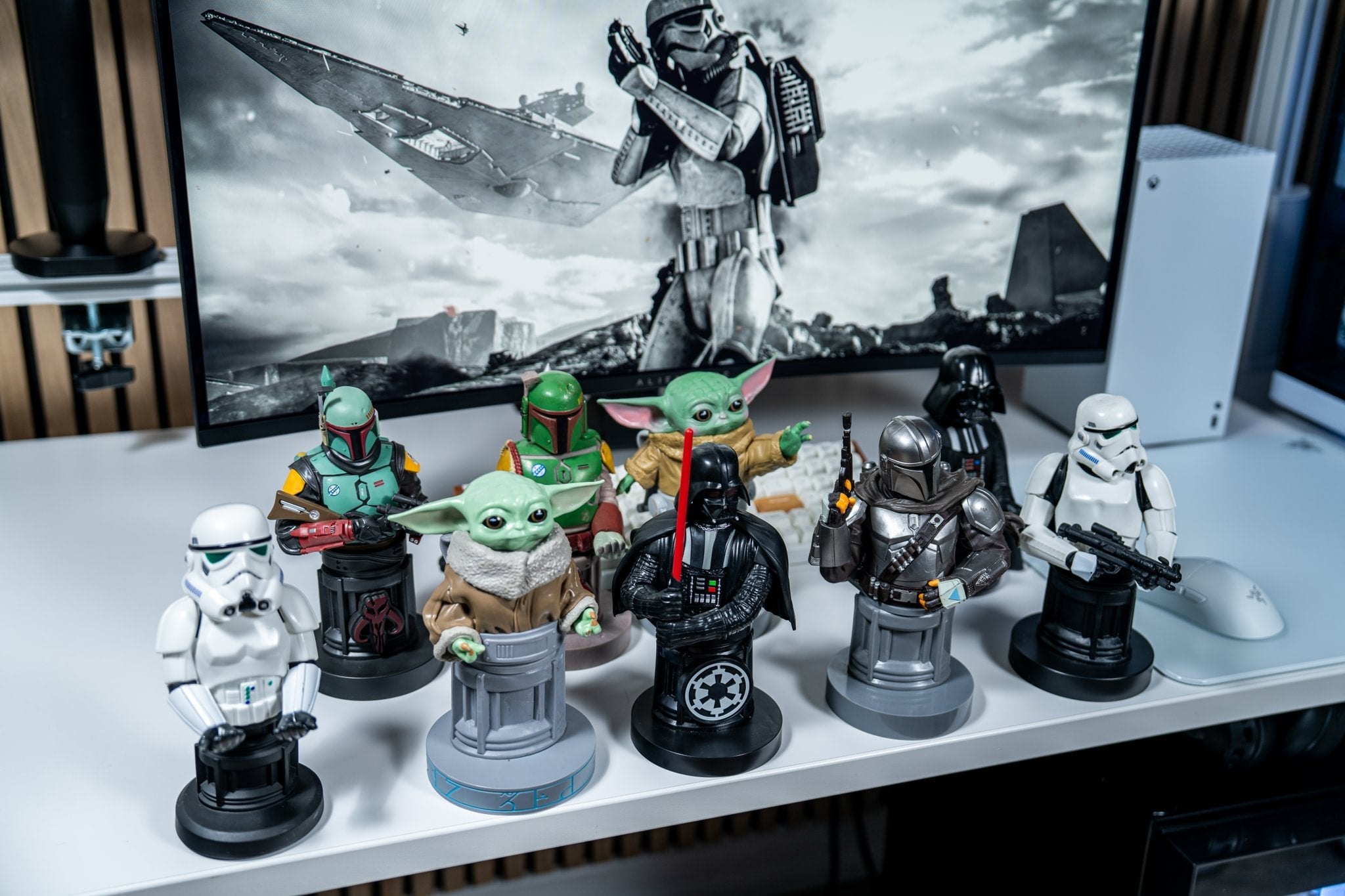 A collection of Star Wars Cable Guys including The Mandalorian, Grogu, Darth Vader, Boba Fett, and Stormtroopers displayed on a white desk in front of a Star Wars-themed monitor setup.