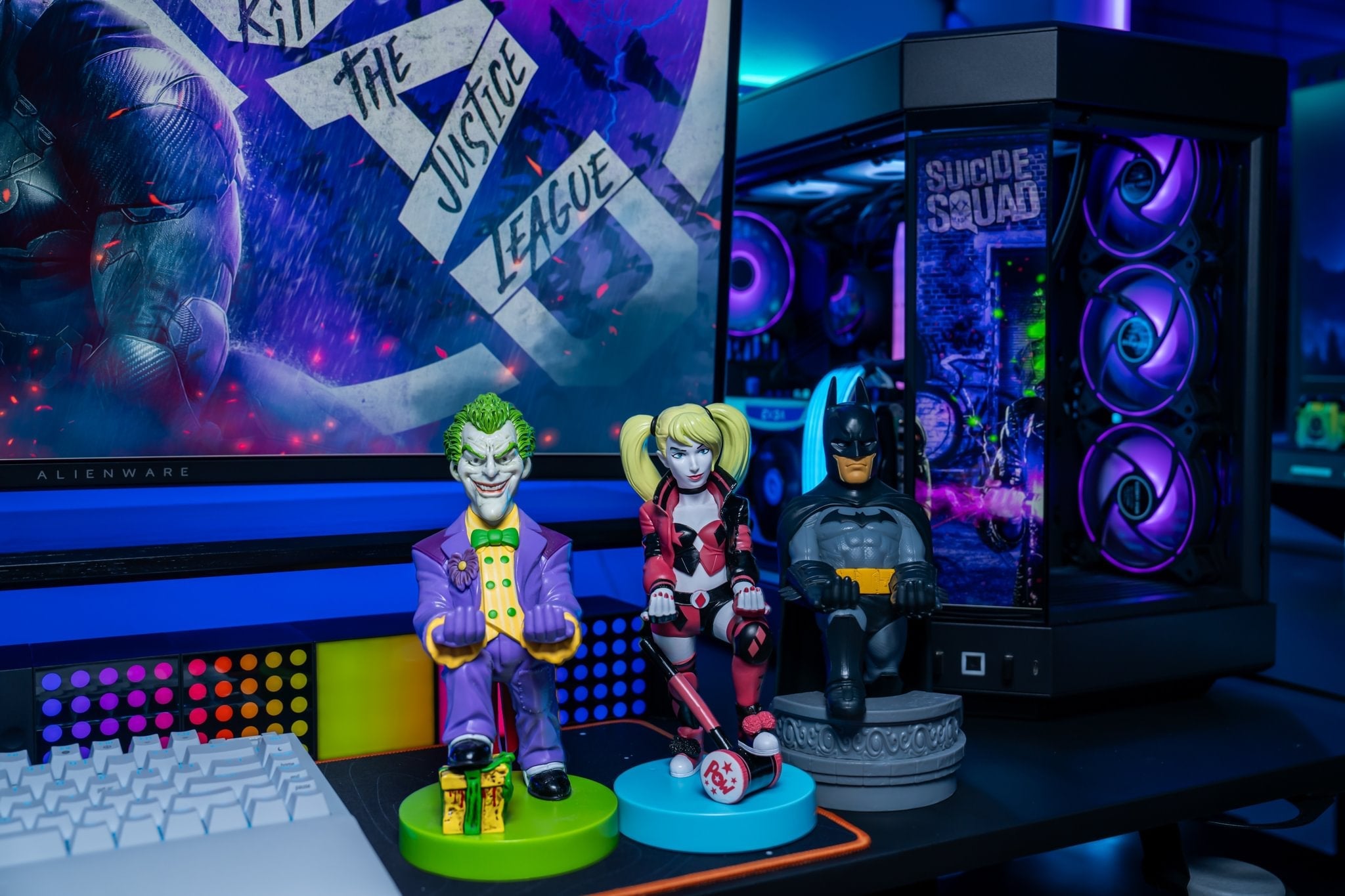 Joker, Harley Quinn, and Batman Cable Guy figures displayed together on a gaming desk with RGB lighting and a Suicide Squad-themed setup in the background.