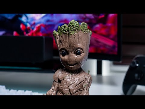 A Cable Guy figure of Toddler Groot standing upright with arms extended to hold a controller or device.